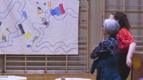 Deux personnes regardent une grande toile accrochée sur une échelle du gymnase. Crédit photo @ Éloi Angers-Roy.