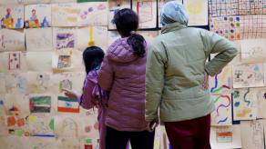 Trois personnes observent un mur recouvert de dessin des jeunes lors du vernissage. Crédit photo @ Éloi Angers-Roy.